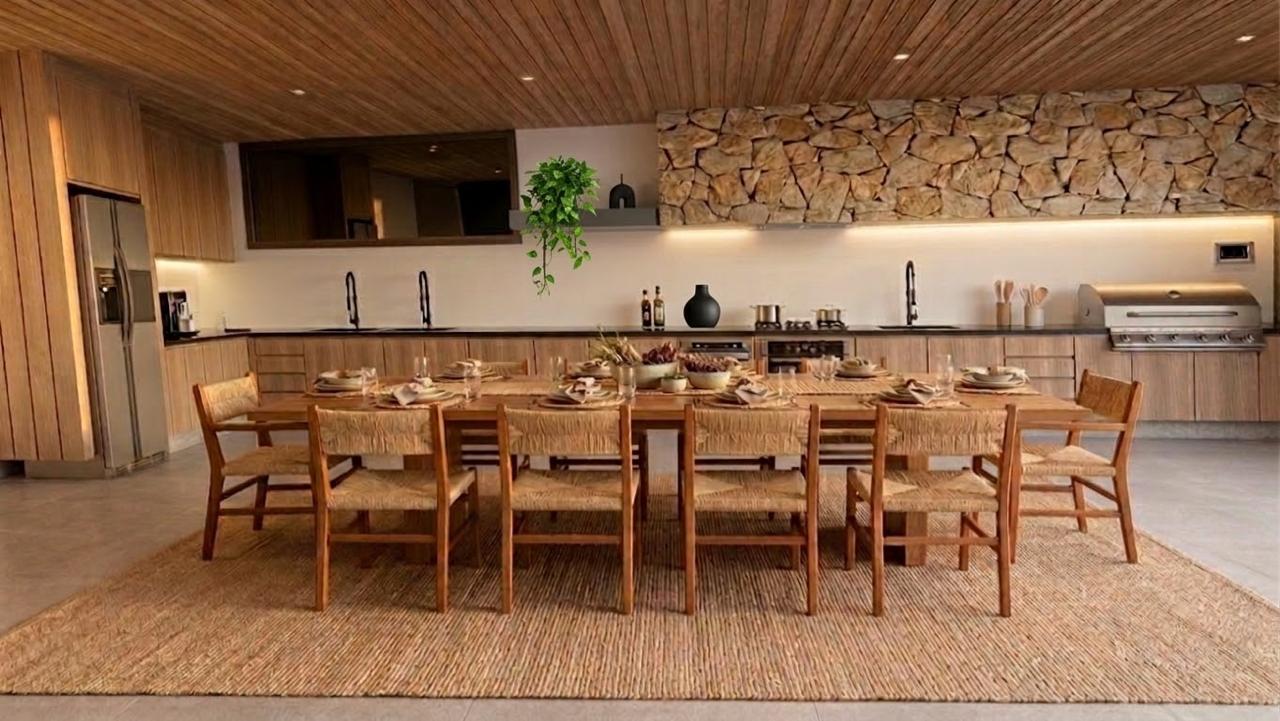Cozinha gourmet integrada à área externa com mesa de madeira, cadeiras em palha, forro de tauari, parede em pedra natural e churrasqueira